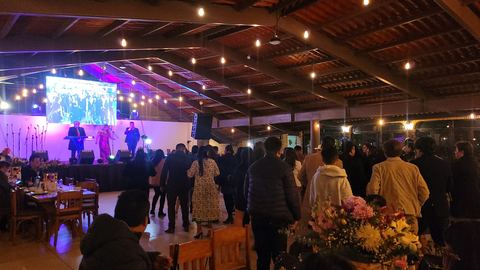 Interior del pabellón durante un evento nocturno, con escenario, pantalla y mesas montadas