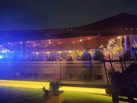 El pabellón techado de Las Palomas encendido de noche, visto desde el jardín, con luces de serie sobre las vigas de madera